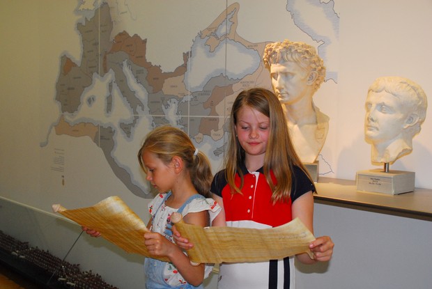 Zwei Mädchen lesen von römischen Schriftrollen.