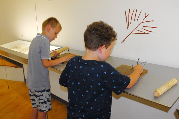 Foto: Zwei Jungen ritzen in römische Wachstafeln.
